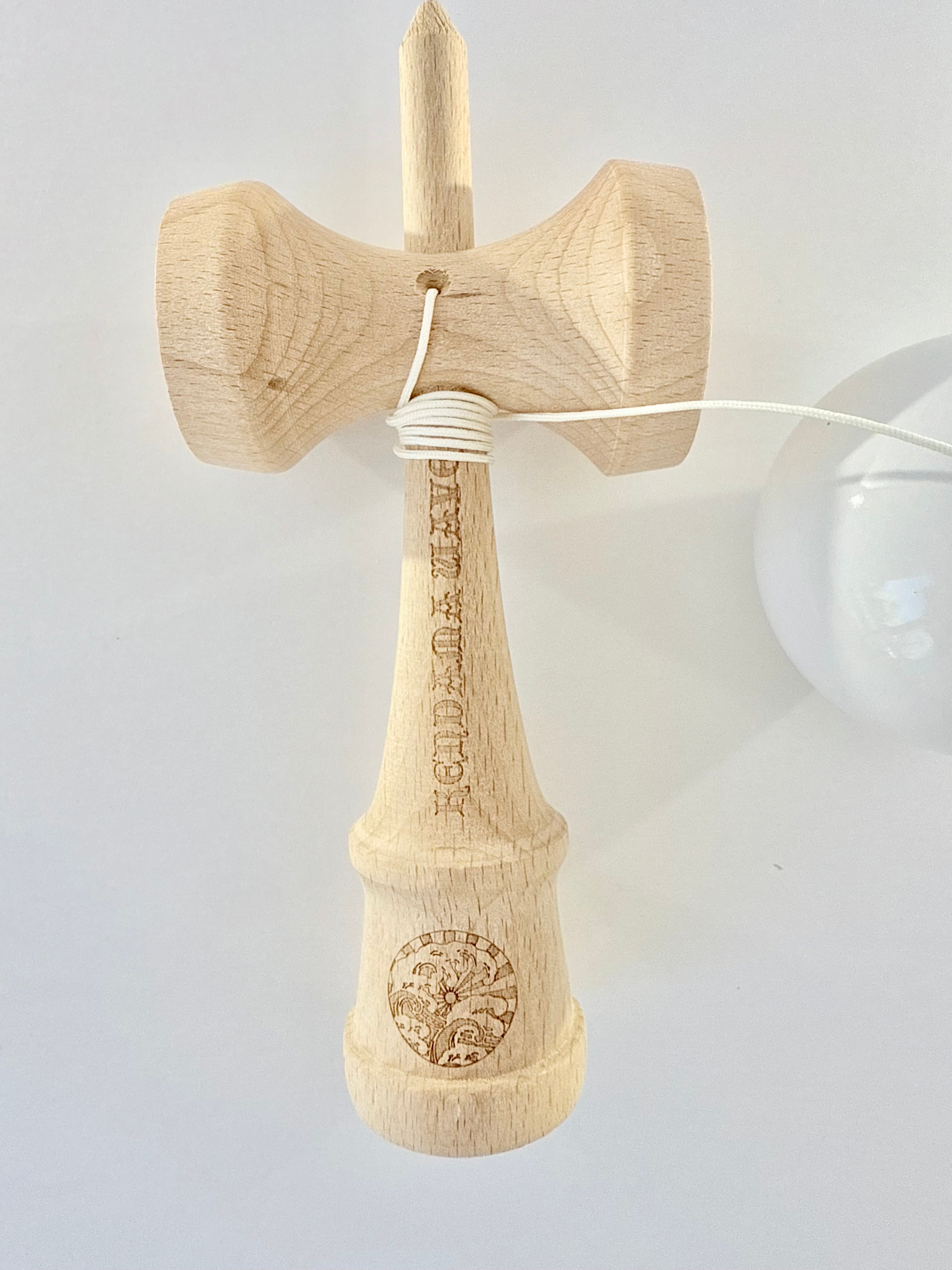 A natural wood kendo sword (shinai) with a white cord, featuring engraved characters and a circular emblem near the base, shown against a plain light background.